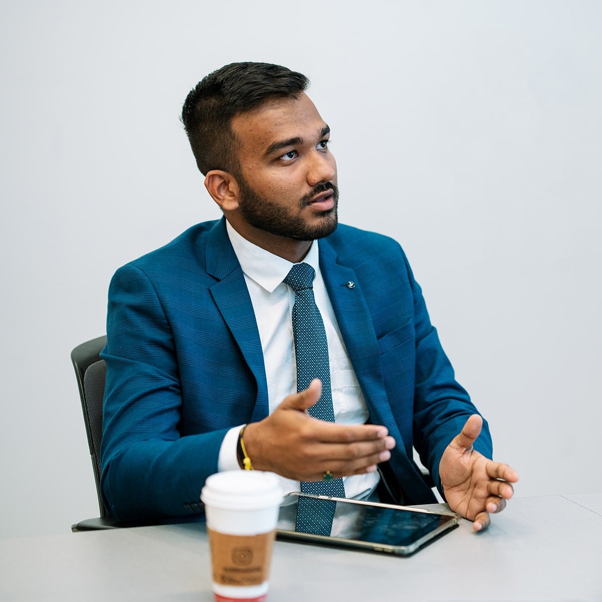 Student in blue suit sitting at table with iPad and coffee cup.