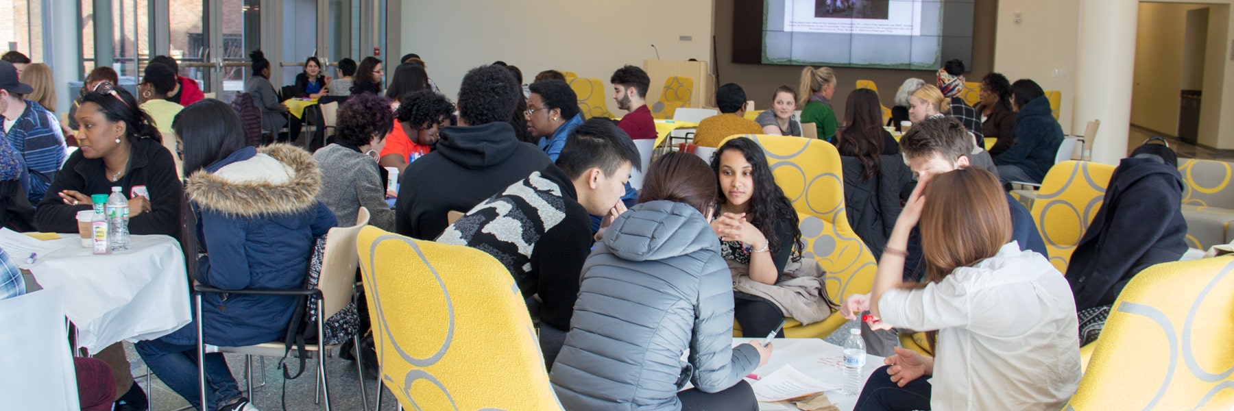 diverse students sitting around multiple tables having discussions