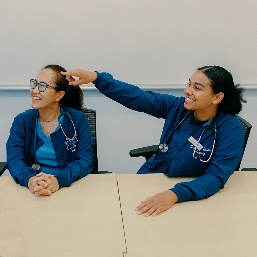 nursing student pointing toward front of class while other student looks on