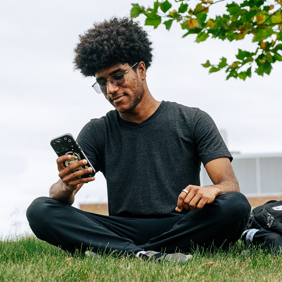 Black student sits under a tree with cell phone