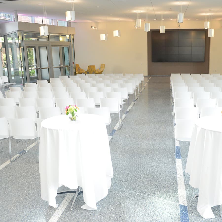 Rows of white chairs and standing tables facing presentation screen.