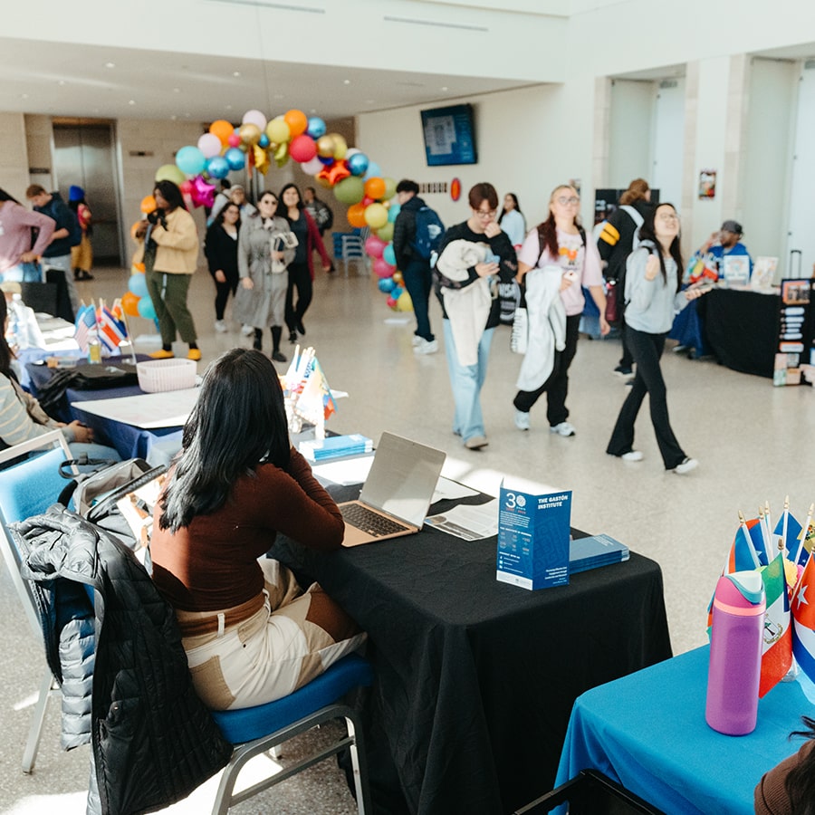 campus center lobby tables with students walking by and balloon arch in background.