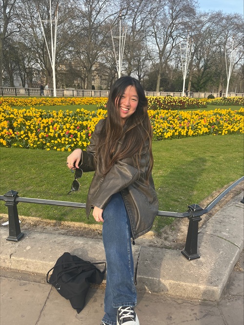 Anya student sitting on bench in front of yellow flowers
