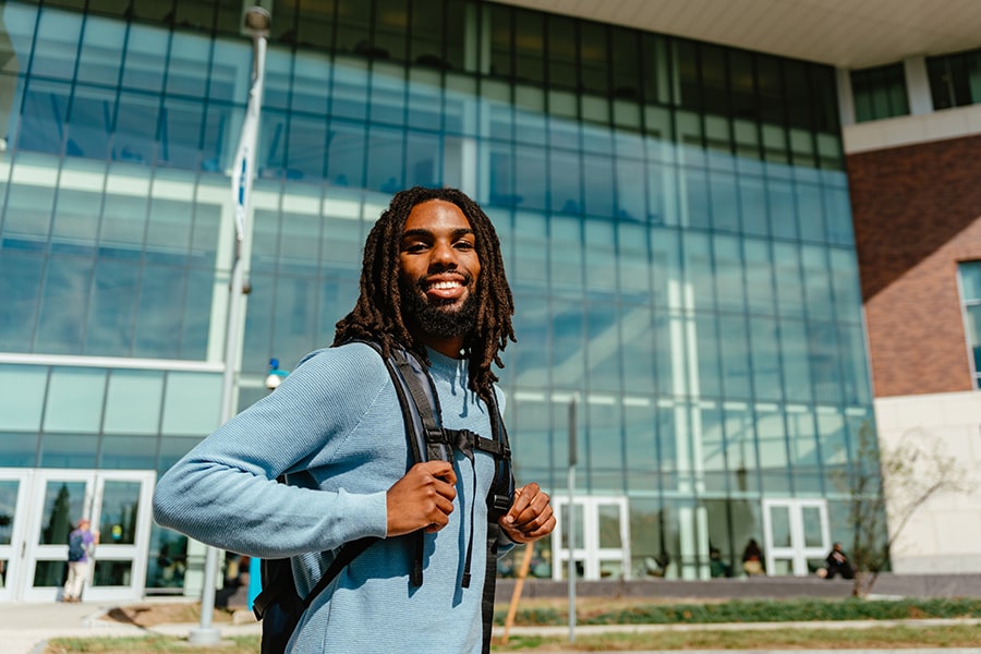 Student wearing a backpack in front of glass building.