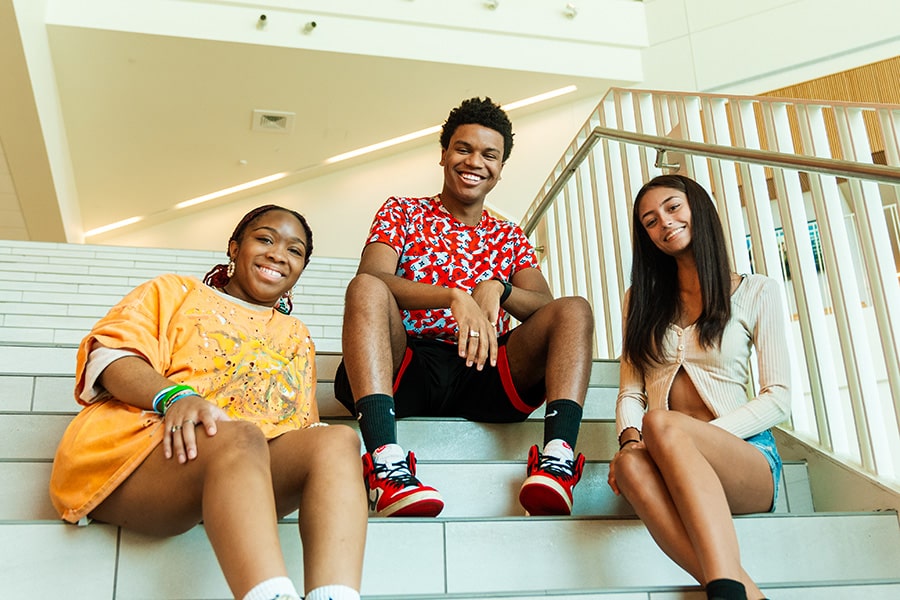 Three UMass Boston students smiling and sitting on the steps in the Integrated Sciences Complex