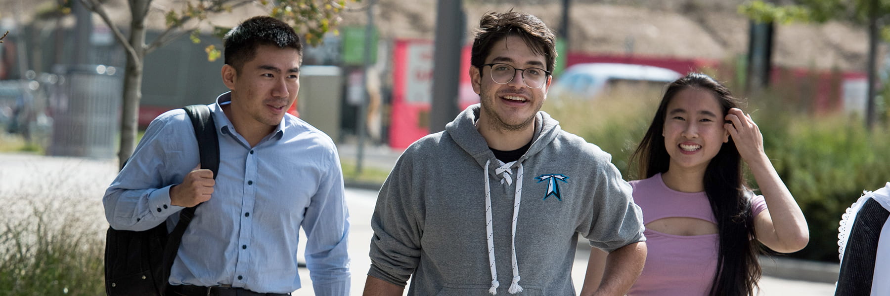 3 students walk outside smiling on campus.