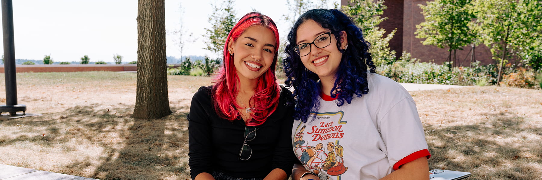 Two students smile sitting on the plaza