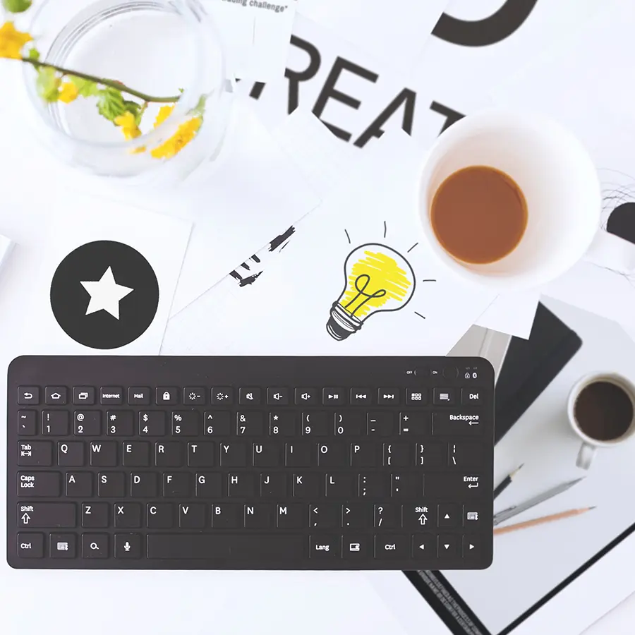 looking down on desktop with keyboard, coffee, writing utensils.